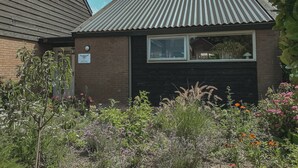 A small building with a metal roof, a window, and a sign on the wall. - A boutique coastal lodge between sea and forest, personally managed by Dutch Sweet Home. With a fireplace, sunny garden and serene atmosphere — created for slow living and true relaxation. (Warmenhuizen)
