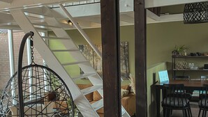 A modern interior with a staircase, a hanging chair, a dining area with chairs, and a table. - A boutique coastal lodge between sea and forest, personally managed by Dutch Sweet Home. With a fireplace, sunny garden and serene atmosphere — created for slow living and true relaxation. (Warmenhuizen)