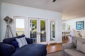 Un salon avec un canapé, un coin repas avec des chaises et une vue à travers des portes vitrées.