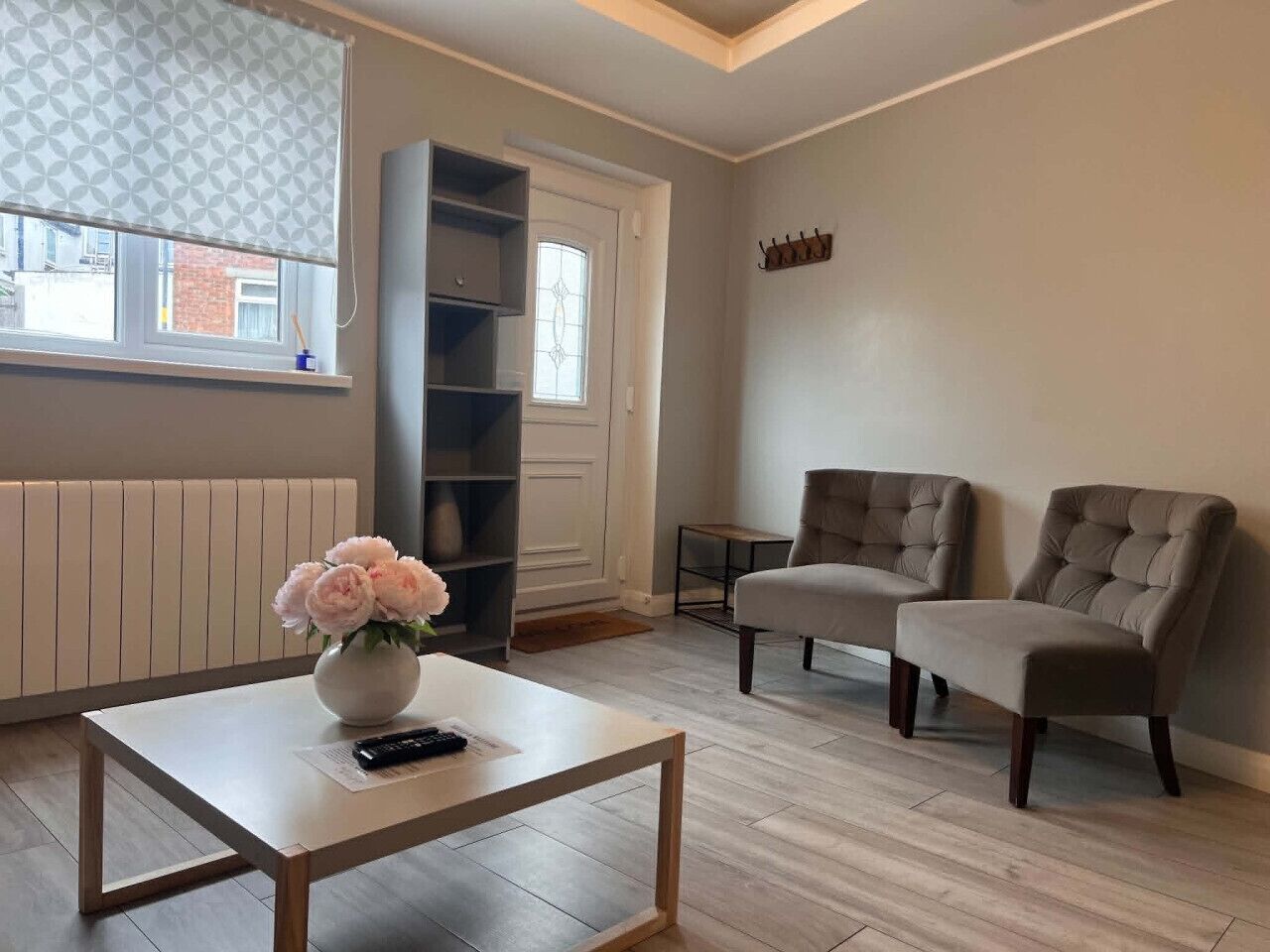 Un salon avec une table basse blanche, un vase de fleurs, deux fauteuils, une bibliothèque et un radiateur.
