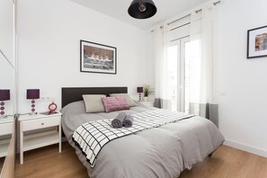 A bedroom with a bed, a nightstand, a wall-mounted picture, a window with curtains, and a door. - Great 4 bedroom Apartment Sagrada Familia (Barcelona)
