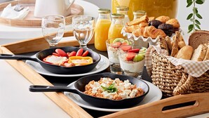 Bandeja de desayuno con huevos revueltos, tostadas, pasteles y un jarro de jugo de naranja.
