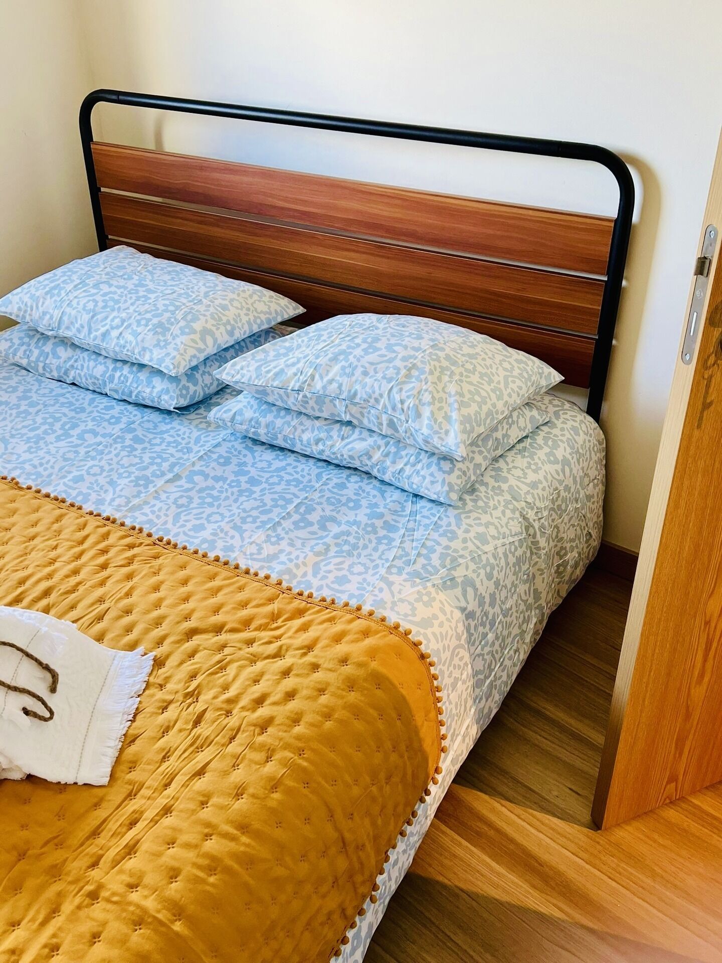 A bed with a wooden headboard, blue patterned pillows, and a yellow quilted bedspread.