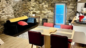 A cozy living area with a stone wall, a black sofa with colorful cushions, a wooden dining table with red chairs, and a view through a glass door. - Douro View House - Breathtaking views of the Douro River (Lamego)