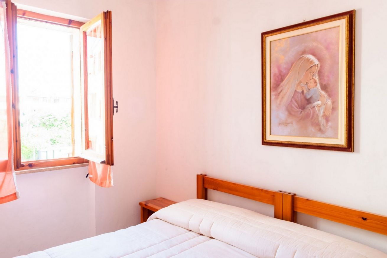 Une chambre à coucher avec un lit, une table de chevet, une fenêtre avec des rideaux et un tableau encadré au mur.