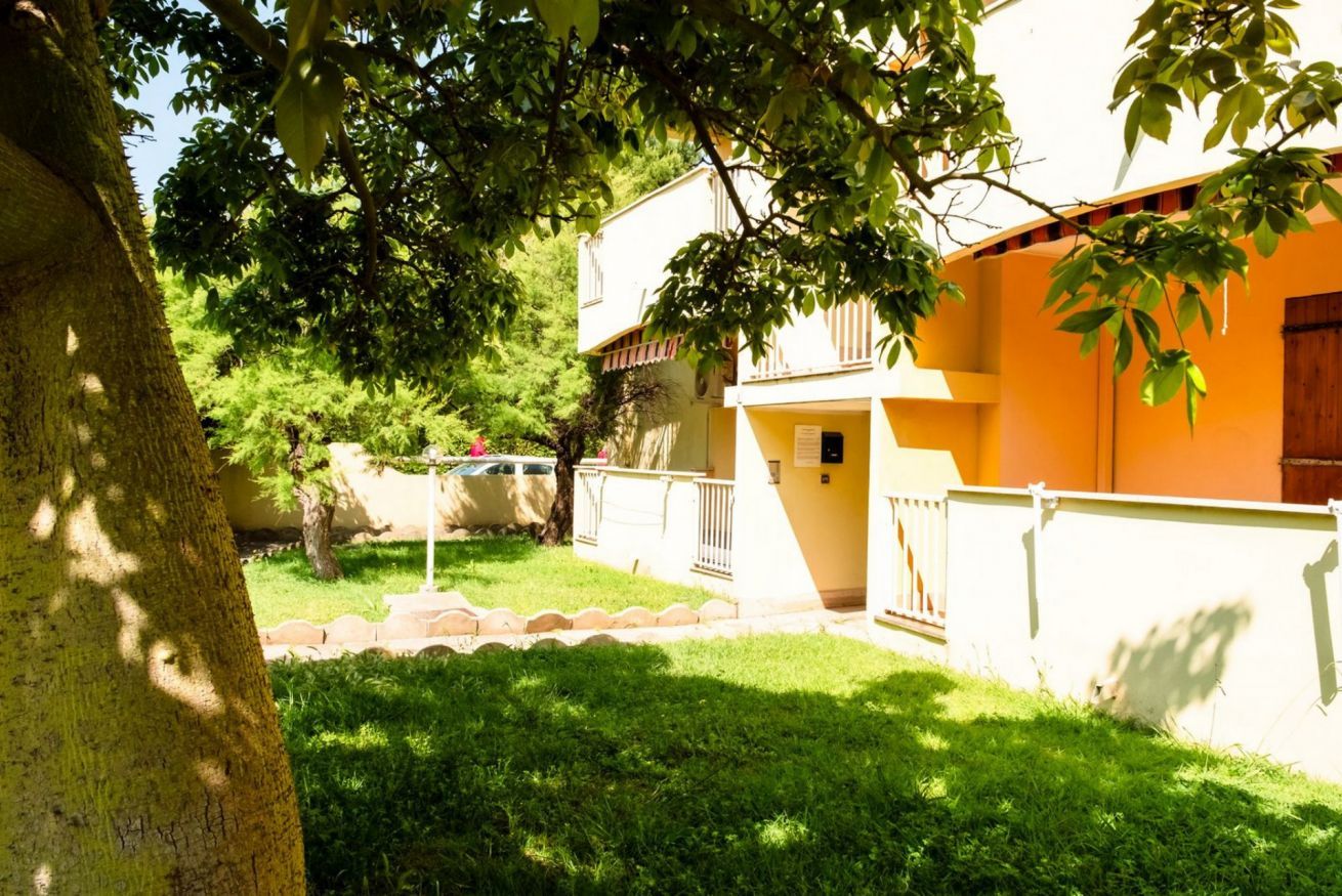 Un edificio de fachada amarilla, un árbol en primer plano y un área verde al fondo.