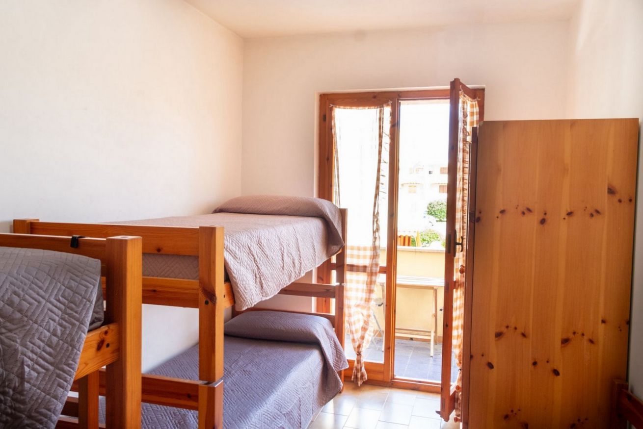 A room with a bunk bed, a wooden wardrobe, and a sliding glass door leading to an outdoor area.