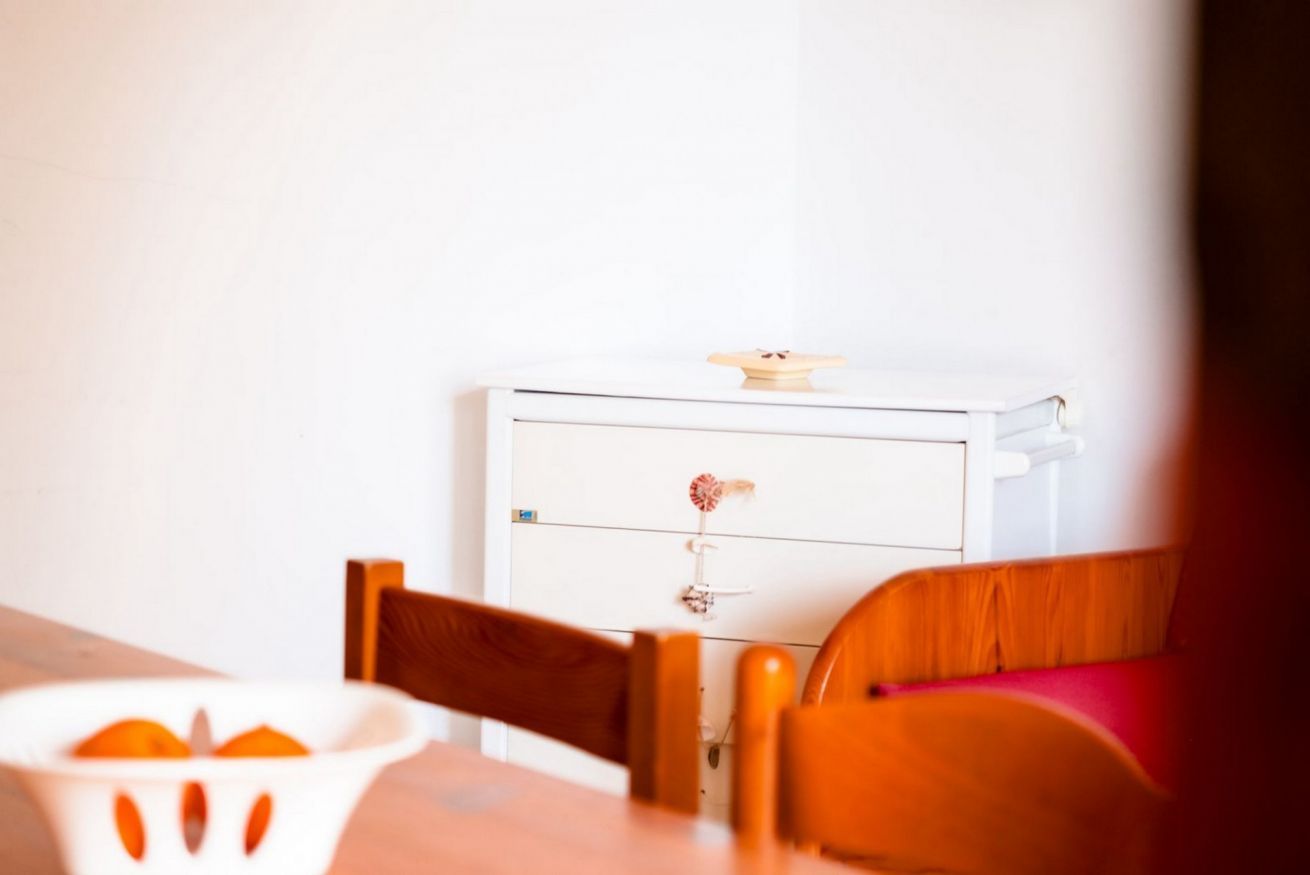 Um quarto com um armário branco, uma cadeira de madeira e uma mesa com uma tigela branca.