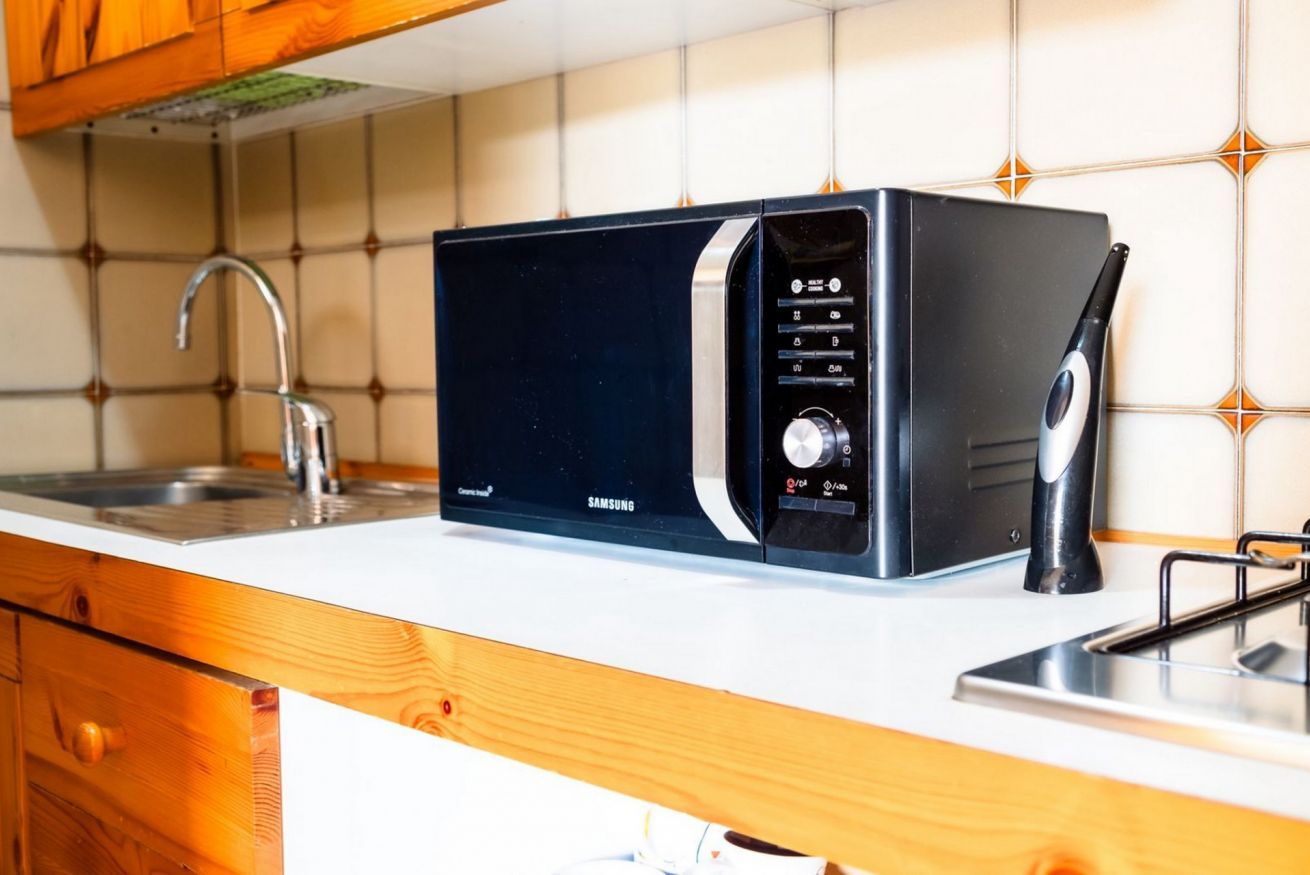 Un microondas Samsung sobre una encimera de cocina con un fregadero y armarios de madera.