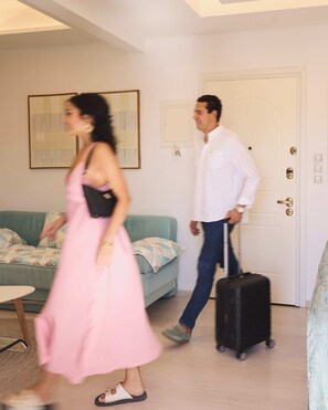 Ein Zimmer mit einer Couch, einem Tisch, einer Tür und einer Person mit einem Koffer.