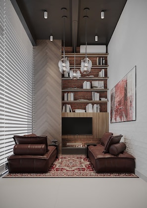 A modern living room with a herringbone wood floor, leather sofas, a red patterned rug, a flat-screen TV, and a brick wall bookshelf.