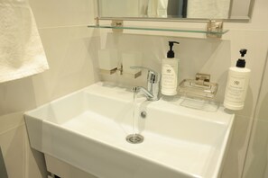 Un baño con un lavabo blanco, un estante de cristal sobre él y dos botellas de jabón para manos.