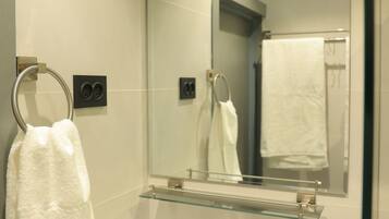A modern bathroom with a white sink, a glass shelf with toiletries, and a large mirror.