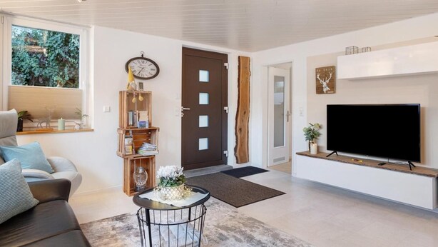 Uma sala de estar moderna com um sofá, uma mesa de centro, uma TV em uma estante de madeira, um relógio e uma porta com design único.