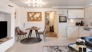 Uma cozinha moderna com armários brancos, uma sala de jantar com mesa e cadeiras redondas, e uma sala de estar com sofá e mesa de centro.