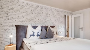 Quarto com parede de tijolos aparentes, cama com roupa de cama estampada e abajur.