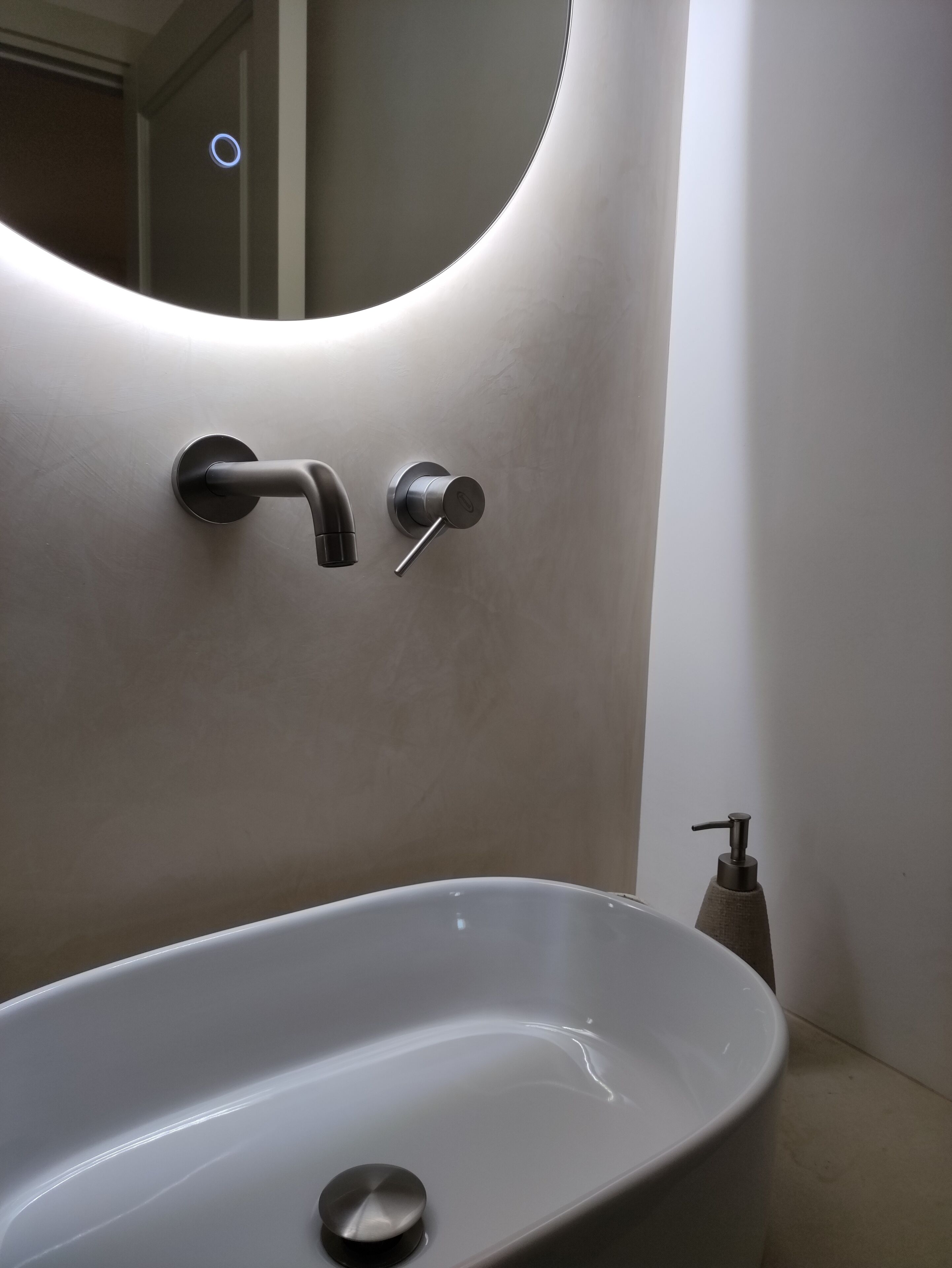 Un baño moderno con un lavamanos ovalado grande, un grifo de pared y un dispensador de jabón.