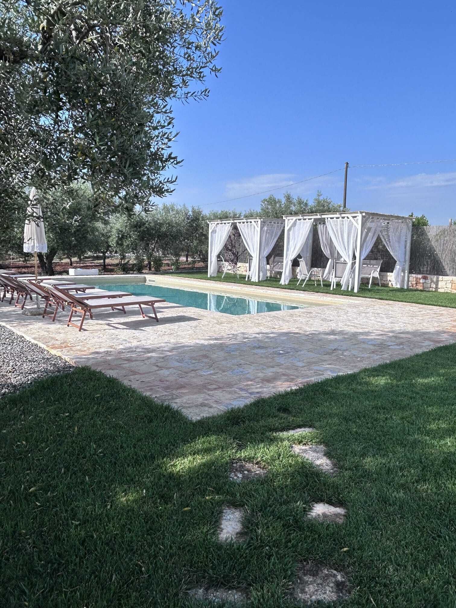 Zona de piscina con sillones de descanso, un espacio de estar techado y un camino de piedra.