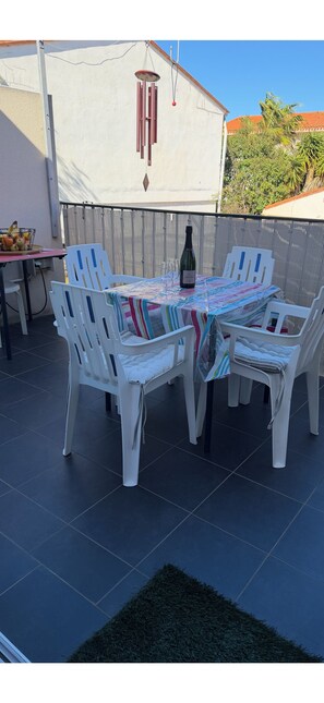 A patio with a table and chairs, a bottle of wine, and a wind chime.