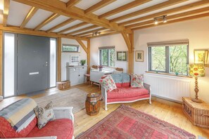 A room with a wooden ceiling, a red sofa, a white table, and a window with a view of trees. - Host & Stay | Tree House (Lewes)