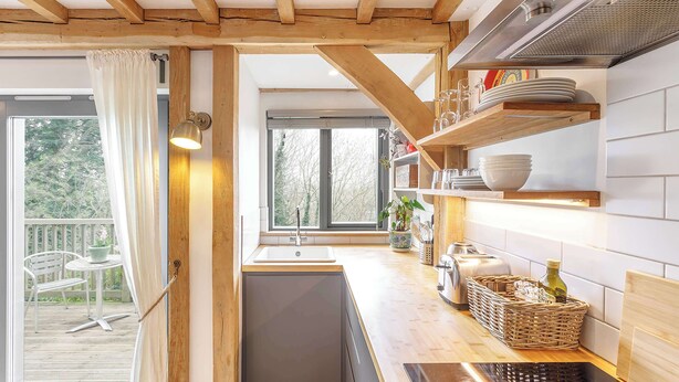 Una cocina con vigas de madera, una ventana, un lavamanos y una encimera con diversos utensilios de cocina.