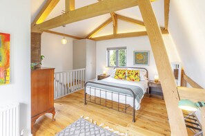 A bedroom with a wooden ceiling, a metal bed frame, a nightstand, a dresser, a window, and a painting on the wall. - Host & Stay | Tree House (Lewes)