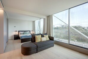 Ein modernes Schlafzimmer mit großem Fenster, einer Couch, einem Bett und einem Nachttisch.