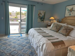 A bedroom with a bed, a nightstand, a lamp, a painting, and a view through a sliding door. - Beachy 2-bedroom townhome in charming New Smyrna Beach with AC (New Smyrna Beach)