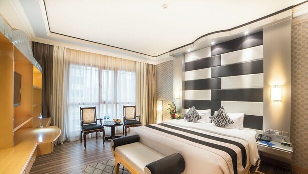 Une chambre d’hôtel avec un grand lit, un bureau, une chaise, un banc et une petite table avec une lampe.