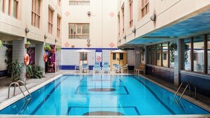 Une piscine intérieure avec un sol carrelé, entourée de murs recouverts de carreaux décoratifs et dotée de fenêtres.