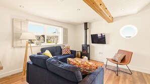 Ein Wohnzimmer mit einer Couch, einem Sessel, einem Fernseher, einem Kamin und einem Fenster mit Rollläden.
