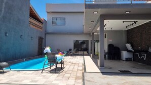 A modern outdoor pool area with lounge chairs and a unicorn float, a reception desk, and a covered walkway. - Maktub House and Leisure Area Temporada Delfinopolis. Cozy space. (Delfinópolis)
