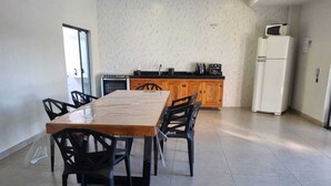 A dining area with a wooden table and chairs, a kitchen with cabinets and appliances, and a white refrigerator. - Maktub House and Leisure Area Temporada Delfinopolis. Cozy space. (Delfinópolis)
