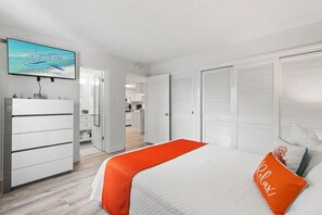 A hotel room with a bed, a TV, a wardrobe, and a view of the kitchen and bathroom. - Beach View 2BR | Walk to Beach & Dining | Sleeps 6 (Panama City Beach)