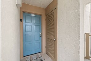 A blue door with a 'C-11' sign, a doormat with 'WELCOME' text, and a beige wall. - Beach View 2BR | Walk to Beach & Dining | Sleeps 6 (Panama City Beach)