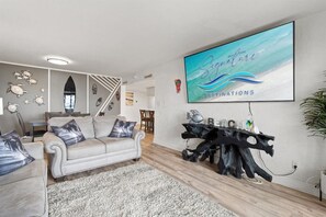 A living room with a sofa, a coffee table, and a TV mounted on the wall displaying 'Signature Destinations'. - Beach View 2BR | Walk to Beach & Dining | Sleeps 6 (Panama City Beach)