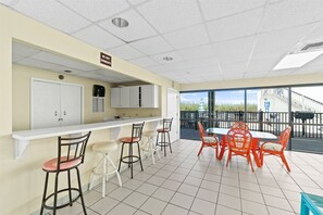 A restaurant with a bar area, high chairs, and a dining table with chairs. - Beach View 2BR | Walk to Beach & Dining | Sleeps 6 (Panama City Beach)