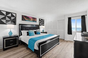 A bedroom with a bed, nightstands, a dresser, and a view of the ocean. - Beach View 2BR | Walk to Beach & Dining | Sleeps 6 (Panama City Beach)