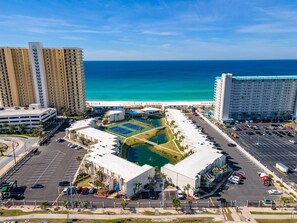 A hotel complex with multiple buildings, a parking lot, and a central courtyard with a pool. - Beach View 2BR | Walk to Beach & Dining | Sleeps 6 (Panama City Beach)