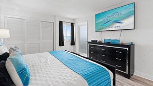 Quarto com cama, penteadeira, televisão e vista para o oceano.