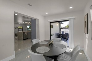 A modern dining area with a round table, white chairs, and a view of the outdoor patio. - Modern Oasis: Hot Tub, Fire Pit, 3 Mi to Beach (Clearwater)