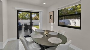 Comedor moderno con una mesa redonda, sillas blancas y vistas al patio trasero a través de un portón corredizo de vidrio.