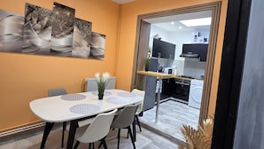A modern dining area with a white table, grey chairs, and a large painting on the wall. - Chambre Autonome Tout Confort with Kitchenette (Roubaix)
