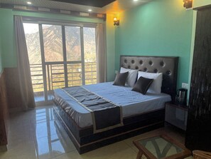 A bedroom with a large bed, a nightstand, a lamp, and a view of mountains through the window.