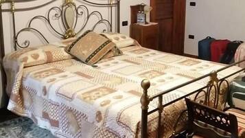 Una cama con una colcha estampada, una mesita de noche pequeña, una silla y una alfombra.