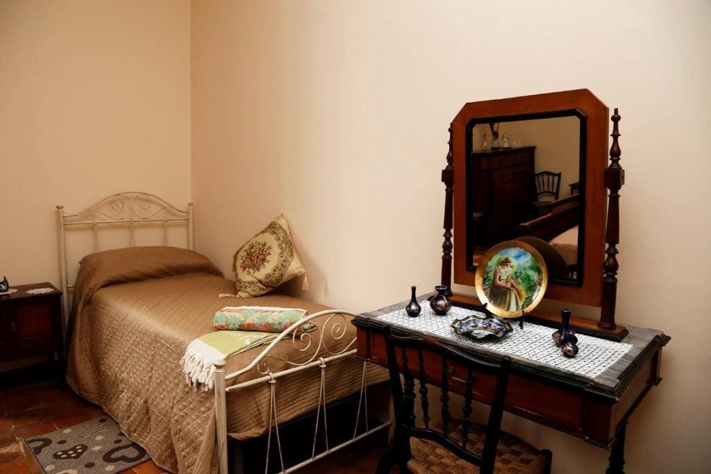 Een slaapkamer met een bed, een houten dressoir, een spiegel en een klein tafeltje.
