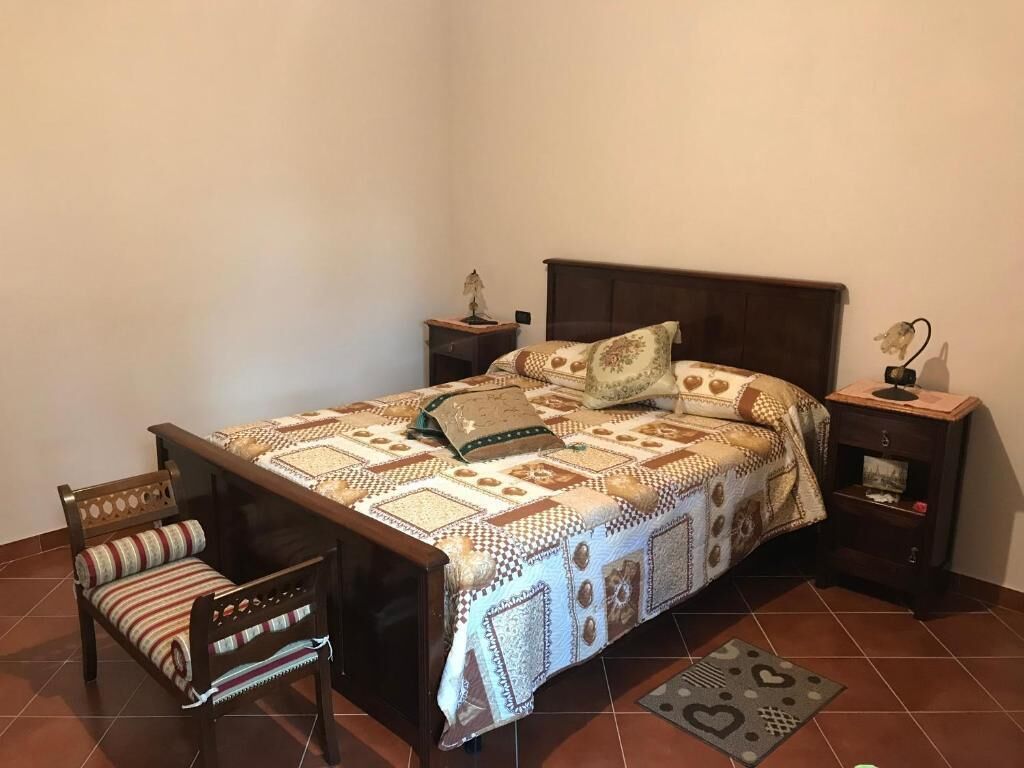 Een slaapkamer met een bed, nachtkastje, stoel en een klein tafeltje.