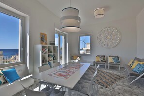 A modern living room with a large window, a dining table, and a sofa. - Abbraccia Mare - panoramic Salento penthouse (Nardò)