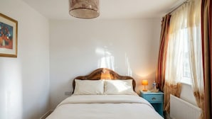 Een keurig opgemaakt bed met een houten hoofdbord, een nachtkastje met een lamp en een raam met gordijnen.