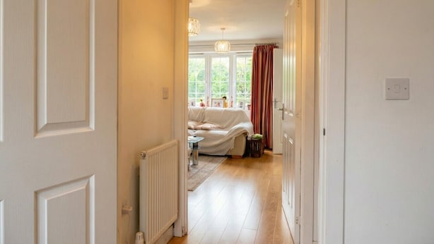 Een gang die leidt naar een slaapkamer met een radiator, een raam met gordijnen en een bed.